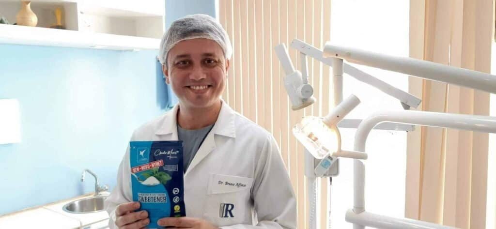Tannlege smilende med utstyr i tannlegeklinikk, klar for behandling.